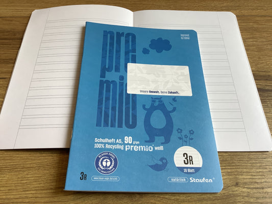 kleines Schulheft mit blauen Cover, einmal geschlossen, darunter einmal aufgeschlagen mit den „Schlauch-Linien“ fürs dritte Schuljahr