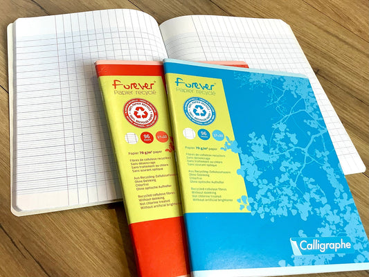 Ein rotes und ein hellblaues Schulheft mit französischer Lineatur, Recyclingpapier, ein aufgeschlagenes Heft