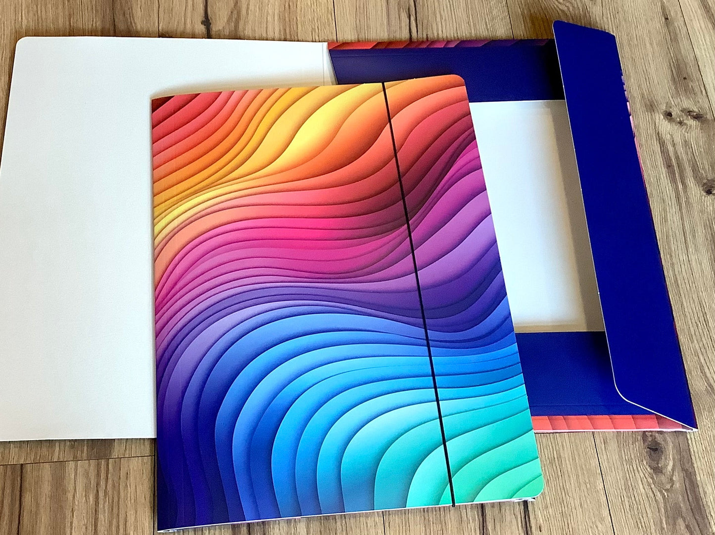 In grafischen Wellen in Regenbogenfarben bedruckte Sammelmappe mit Gummizug aus Recyclingpappe.
Erhältlich bei Polly Paper - umweltfreundlicher Schulbedarf in Berlin-Mitte