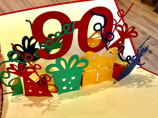 dreidimensionale Pop-up-Karte zum 90. Geburtstag - eine 90 klappt sich beim Öffnen auf, daneben Geschenke und Luftschlangen.
Erhältlich bei Polly Paper in Berlin-Mitte