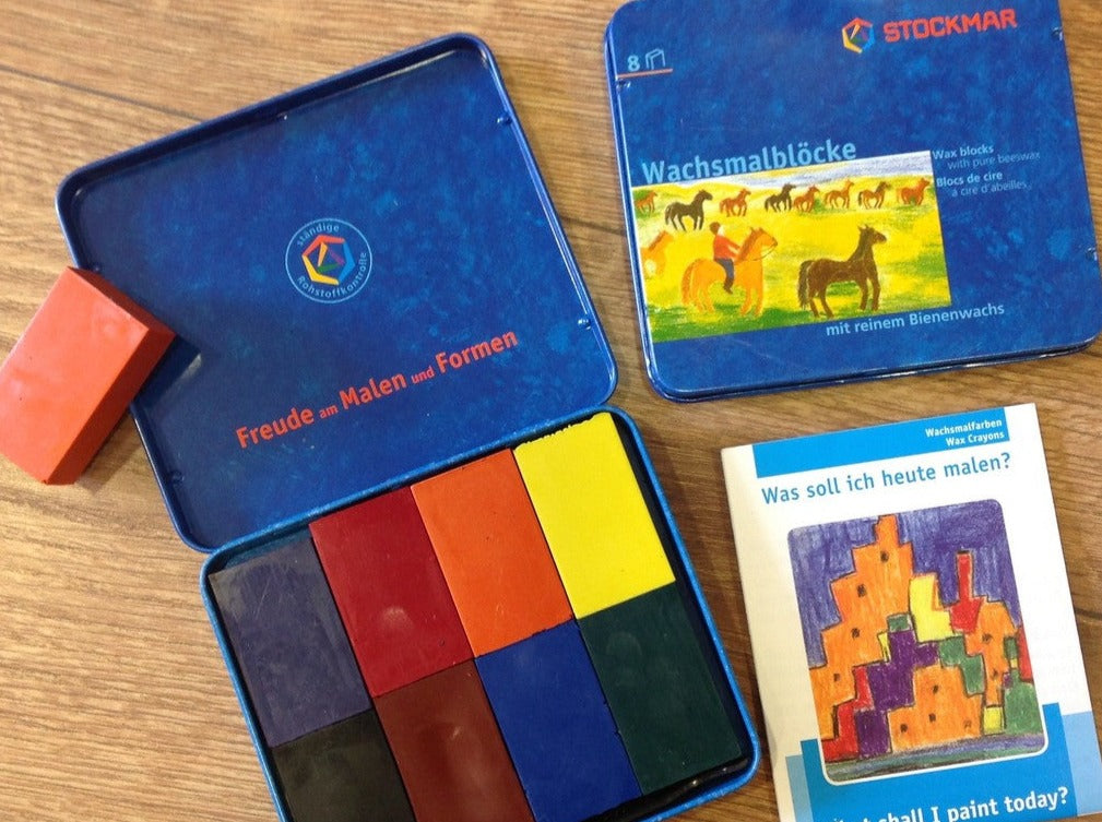 8 Wachsmalblöcke in einem Blechetui: rot, orange, gelb, grün, blau, braun, lila und schwarz