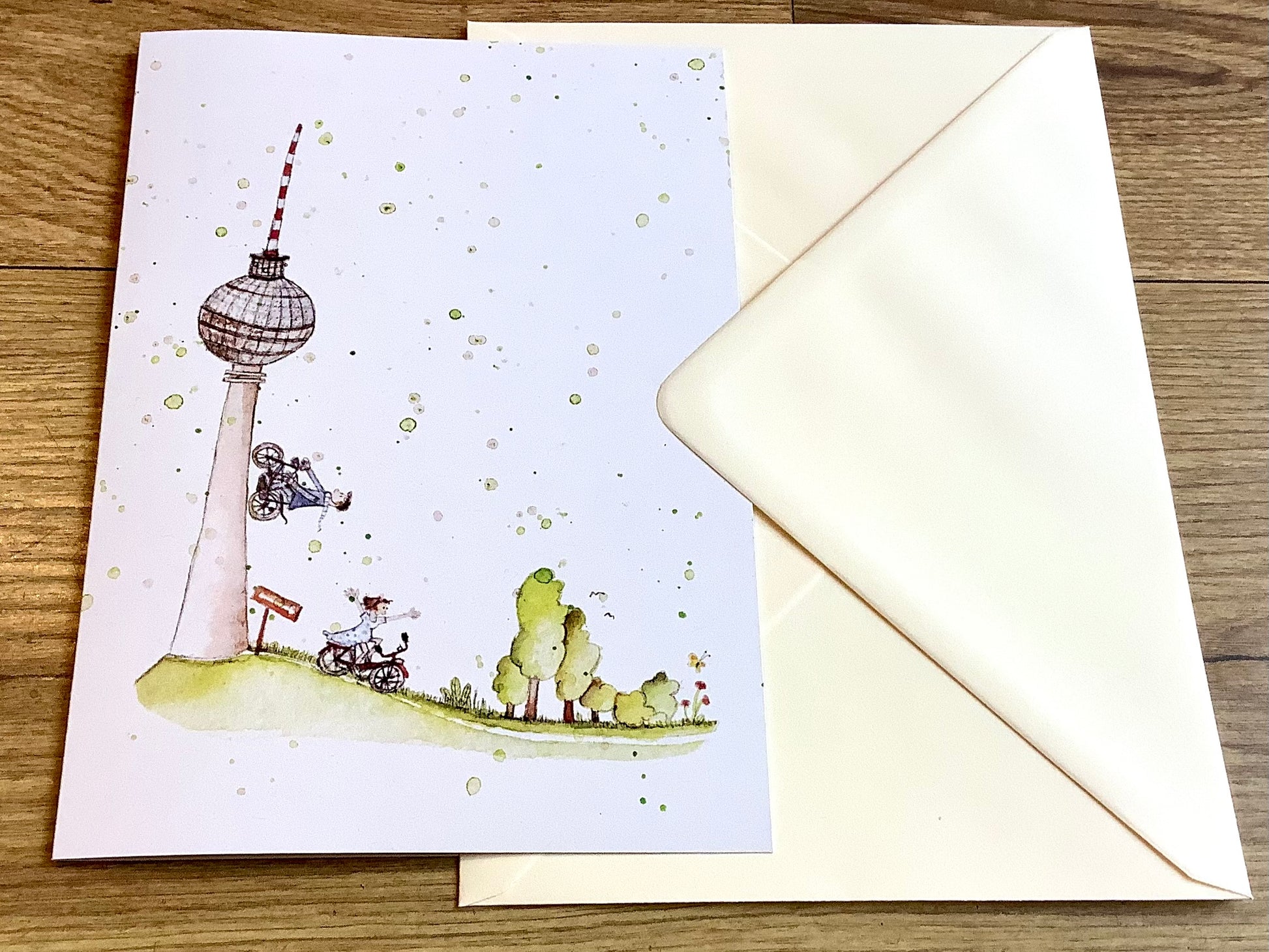 Große Klappkarte mit dem Berliner Fernsehturm , einem Jungen, der mit dem Rad am Turm hochfährt und einem Mädchen auf dem Rad mit ausgebreiteten Armen.