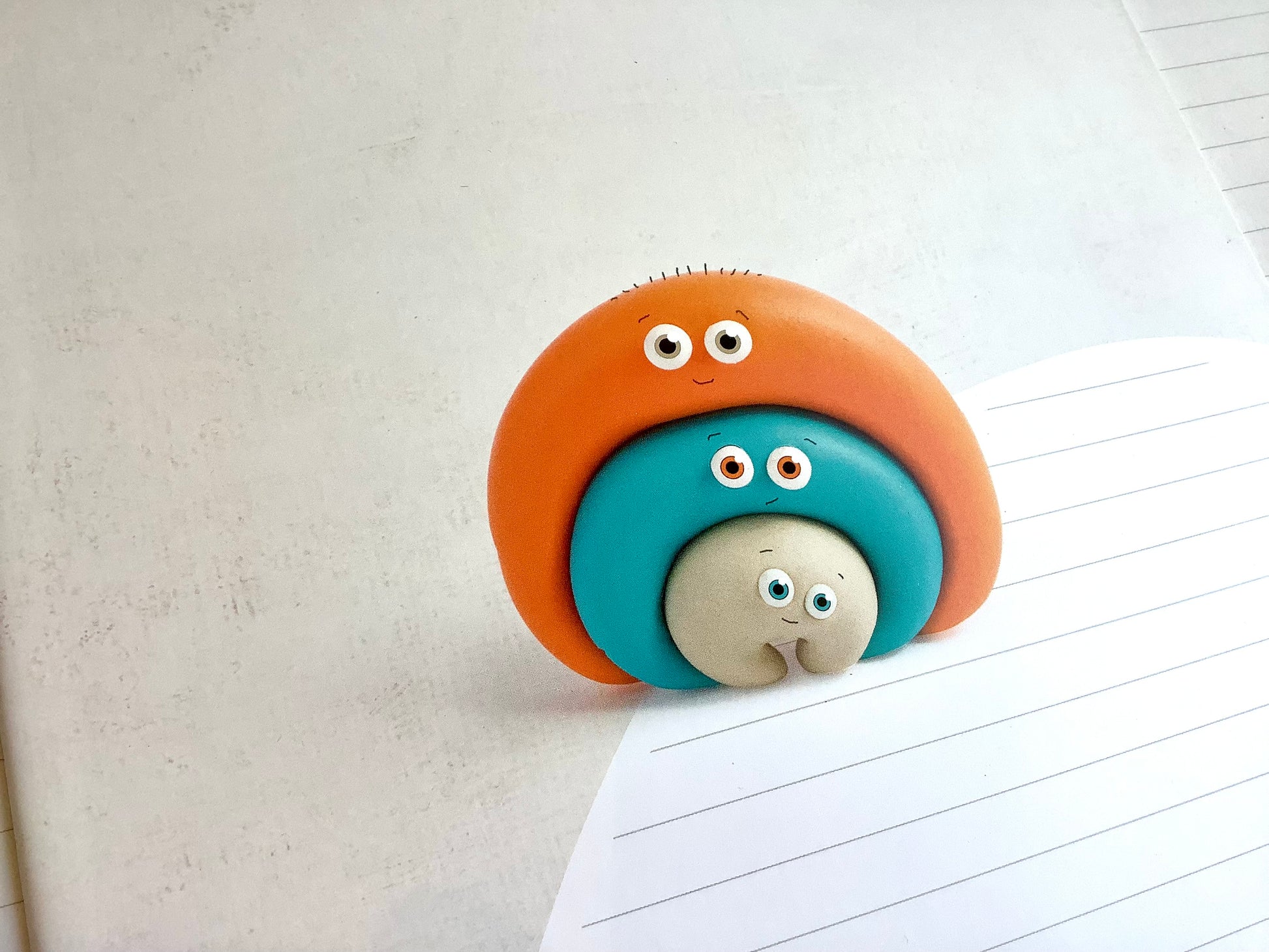 Ein liniertes Heft, das nicht nach Schule aussieht: süße bunte Knetfigur (Fantasiefigur) mit lächelndem Gesicht auf dem Cover. Weiß, liniert.