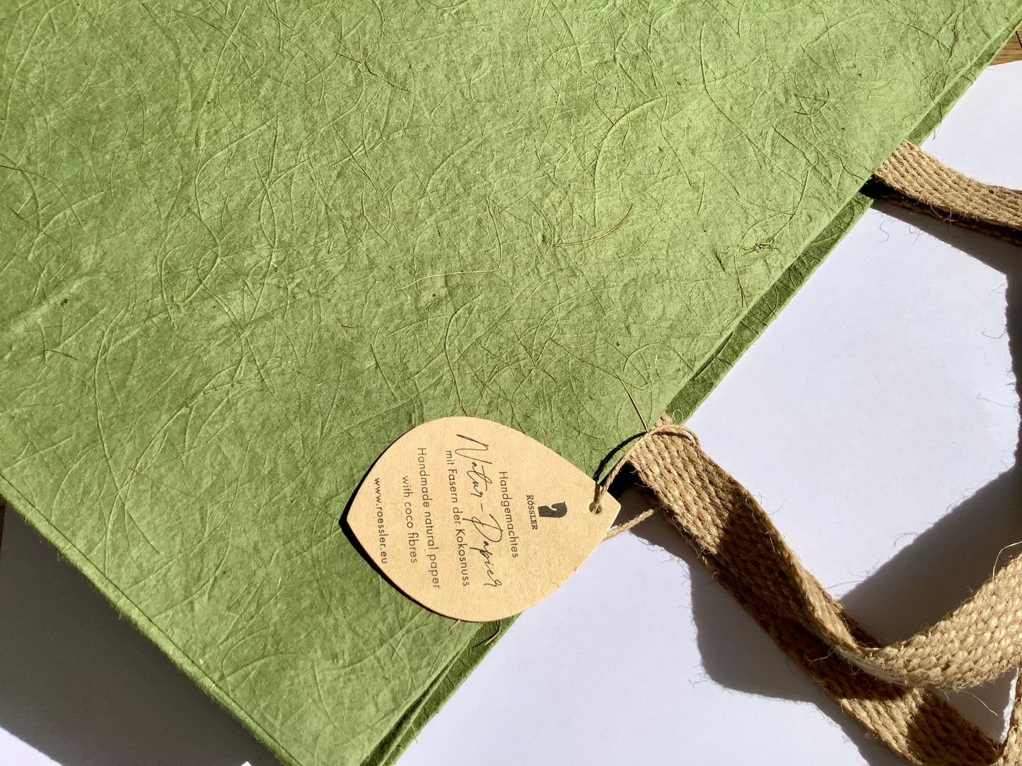 Grüne Geschenktasche aus Naturpapier mit Kokosfasern und Jute-Henkeln.