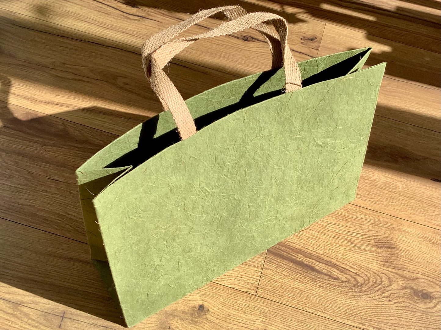 Grüne Geschenktasche aus Naturpapier mit Kokosfasern und Jute-Henkeln.