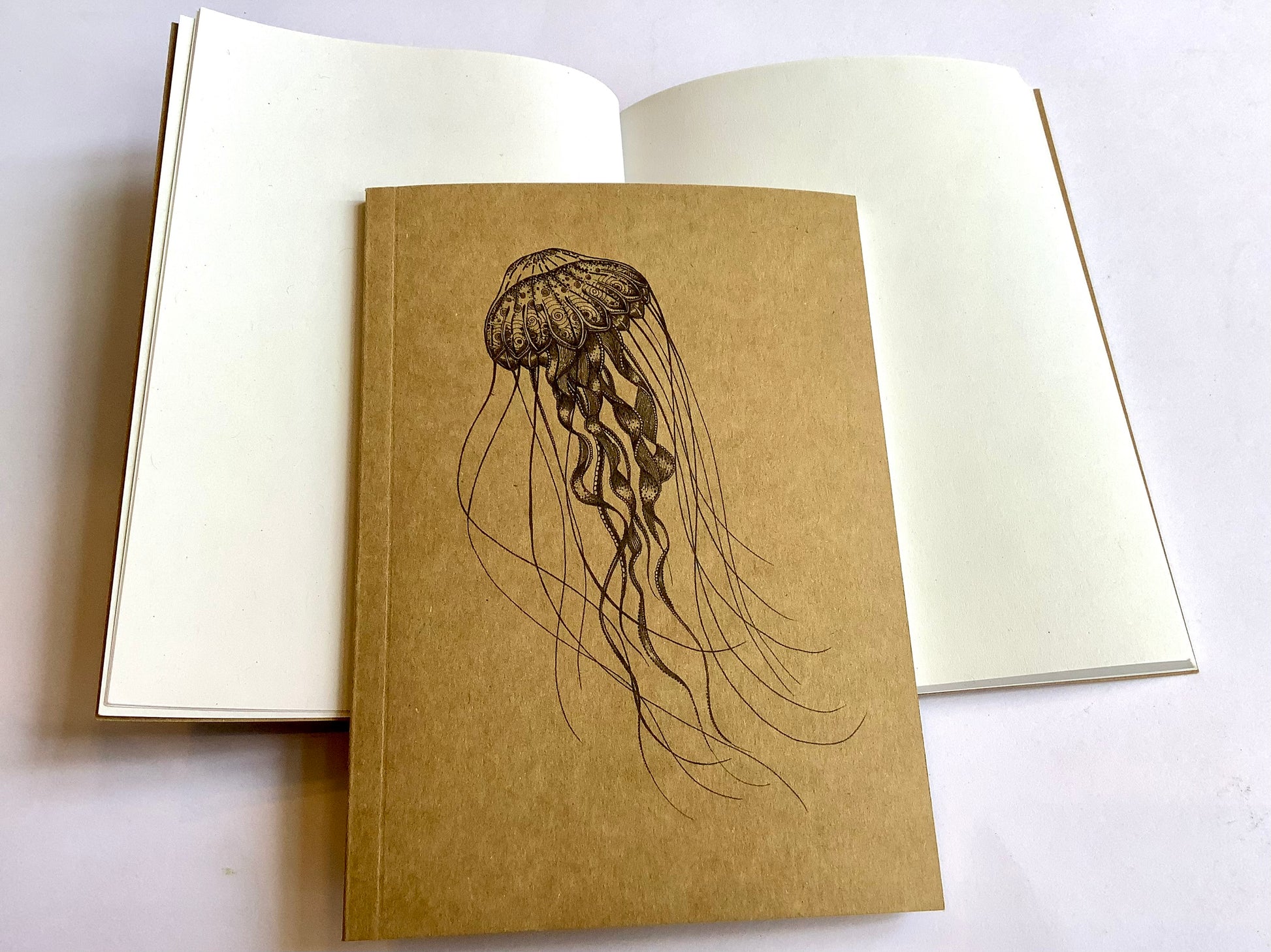kraftfarbenes kleines Notizbuch mit einer schwarz gezeichneten filigranen Tiefseequalle auf dem Cover, innen weißes Papier, unliniert. Recyclingpapier.