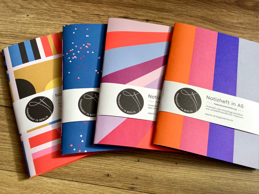 Fadengeknüptes Notizheft im A5-Hochfomat mit einem Cover aus bunt gemustertem Papier, innen unliniertes farbiges Recyclingpapier