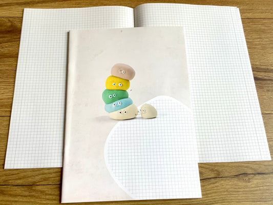 Ein kariertes Heft, das nicht nach Schule aussieht: süße bunte Knetfigur (Fantasiefigur) mit lustigem Gesicht auf dem Cover. Weiß, kariert mit schmalem Rand, durch eine Linie abgetrennt.