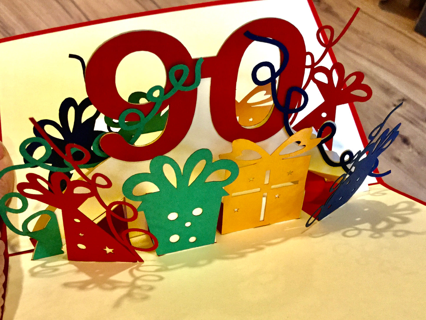  dreidimensionale Pop-up-Karte zum 90. Geburtstag - eine 90 klappt sich beim Öffnen auf, daneben Geschenke und Luftschlangen. 
Erhältlich bei Polly Paper in Berlin-Mitte