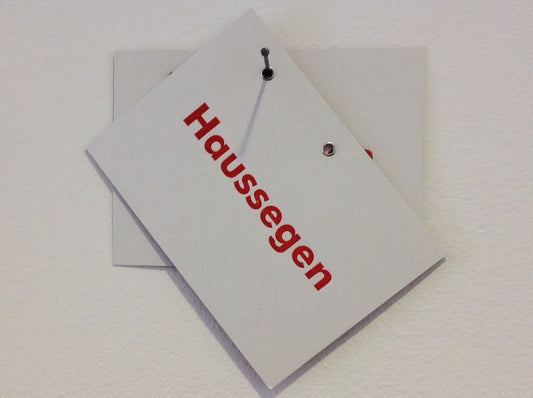 Postkarte "Haussegen" hängt schief am Nagel in einer von 2 Ösen zum Aufhängen