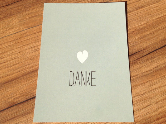 minimalistische Dankes-Postkarte : DANKE in Großbuchstaben, schwarz, kleines weißes Herz auf mintfarbenem Hintergrund
