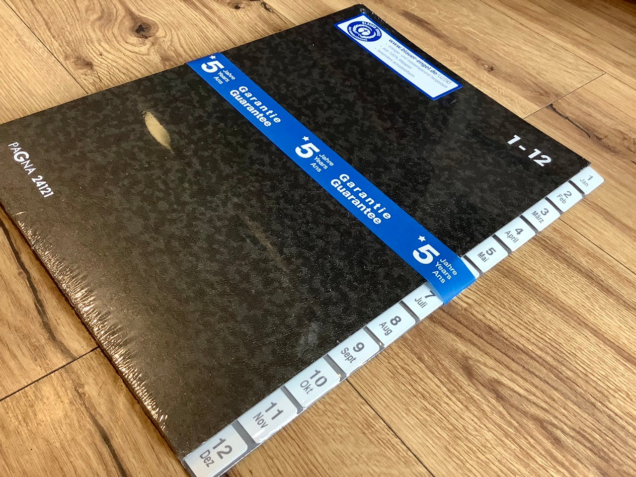 Pultordner schwarz (Wolkenmarmor), dicker Karton, innen 12 Fächer, seitliche weiße Taben, beschriftet mit den Zahlen 1 bis 12 und den 12 Monaten